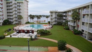 Un patio de hotel con piscina, mobiliario exterior y vista al agua.