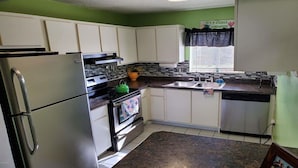 Una cocina compacta con gabinetes blancos, un refrigerador, una estufa y un lavavajillas.