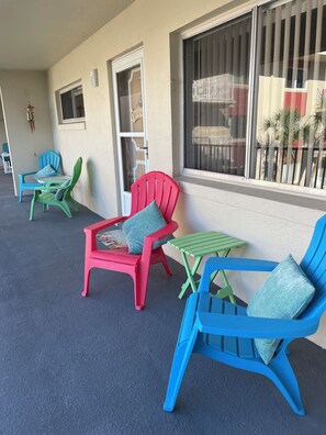 An outdoor seating area with plastic chairs and tables, a door with a sign, and a window with bars. - Beachside condo with a view of the Halifax river ,  Snowbirds paradise. (Daytona Beach)