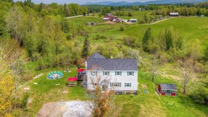 A large house with a red barn, surrounded by a green field and trees. - Vermont Vacation Rental: Hot Tub, Near Ski Resorts (Mt Holly)