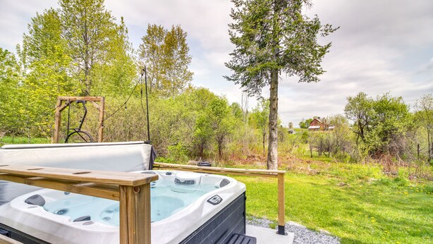 A hot tub on a wooden deck with a view of a grassy area and trees. - Vermont Vacation Rental: Hot Tub, Near Ski Resorts (Mt Holly)