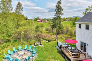 A backyard with a fire pit, outdoor seating, and a deck with a table and chairs. - Vermont Vacation Rental: Hot Tub, Near Ski Resorts (Mt Holly)