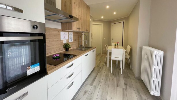 A modern kitchen with a built-in oven, a wooden cabinet, and a white dining table with chairs.