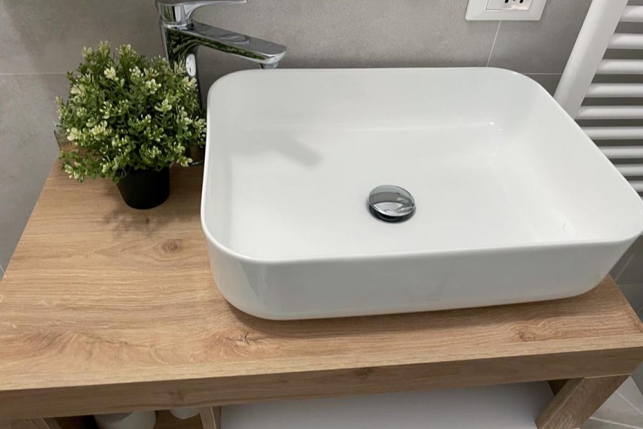 A bathroom with a white sink on a wooden countertop, a potted plant, and a modern faucet.