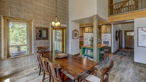 A spacious dining area with a large wooden table and chairs, a stone wall, and a view of the outdoors.