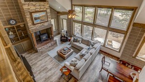 A spacious living area with a stone fireplace, a large window offering a view of the outdoors, and a modern ceiling fan.
