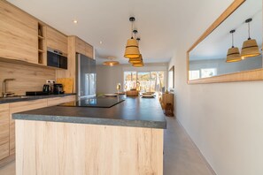 A modern kitchen with wooden cabinetry, a central island, and pendant lighting. - Villa Roquille, direct beach access (Agde)