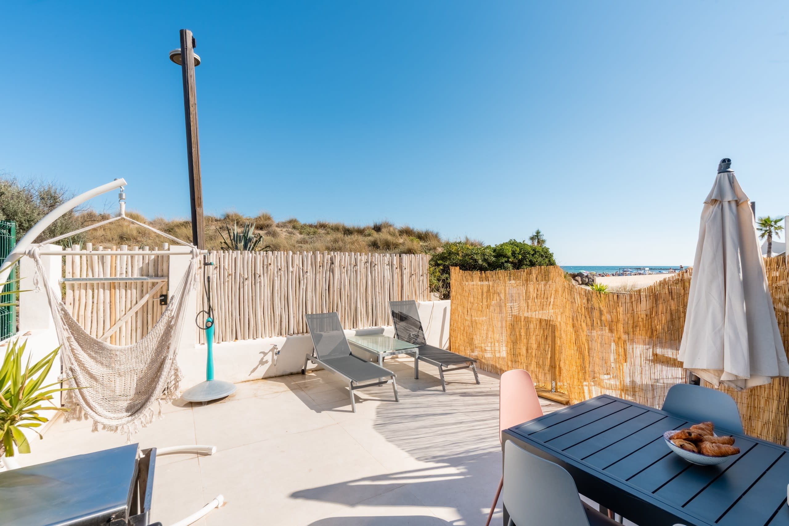 Eine Außenpatio mit Lounge-Möbeln, einem Tisch mit einer Schale Gebäck und Blick auf den Strand.