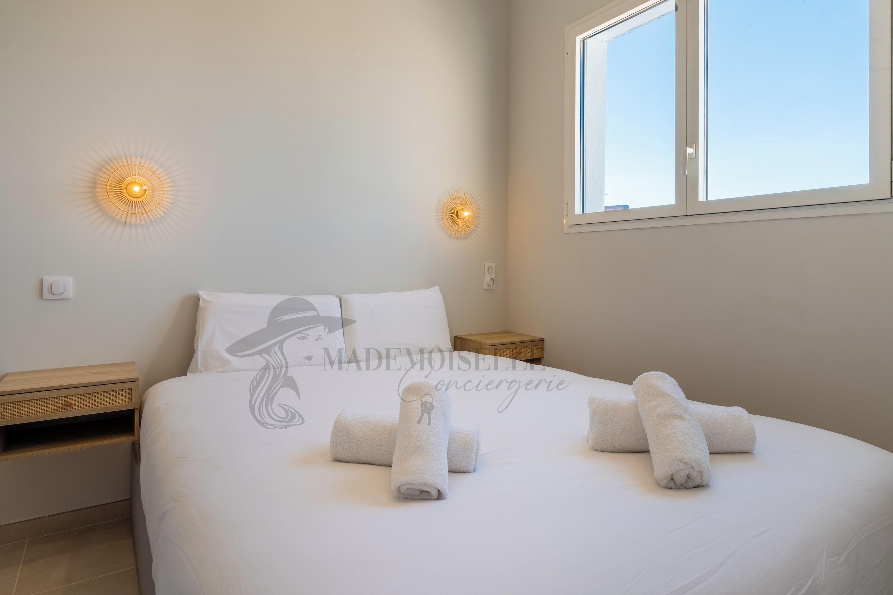 A bedroom with a bed, two wall-mounted lights, a window, and a nightstand.