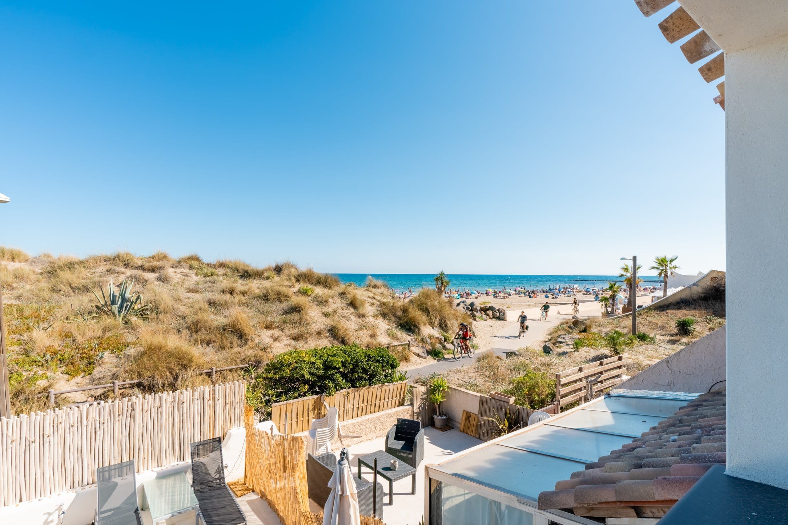 Un balcon avec vue sur la plage, des sièges d’extérieur et un ciel dégagé.