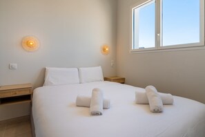 A bedroom with a bed, two wall sconces, a window, and a nightstand.