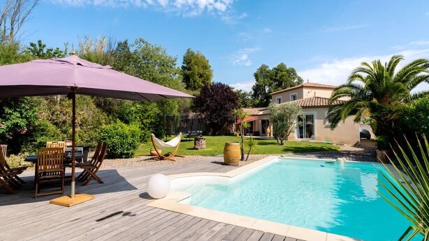 A swimming pool with a wooden deck, outdoor furniture, and a hammock.