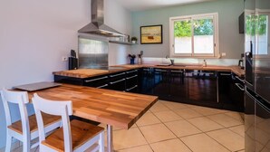 A modern kitchen with a wooden table, white chairs, a stainless steel range hood, and a large window.
