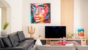 A modern living room with a black leather sofa, a grey couch, a flat-screen TV, and a colorful abstract painting on the wall.