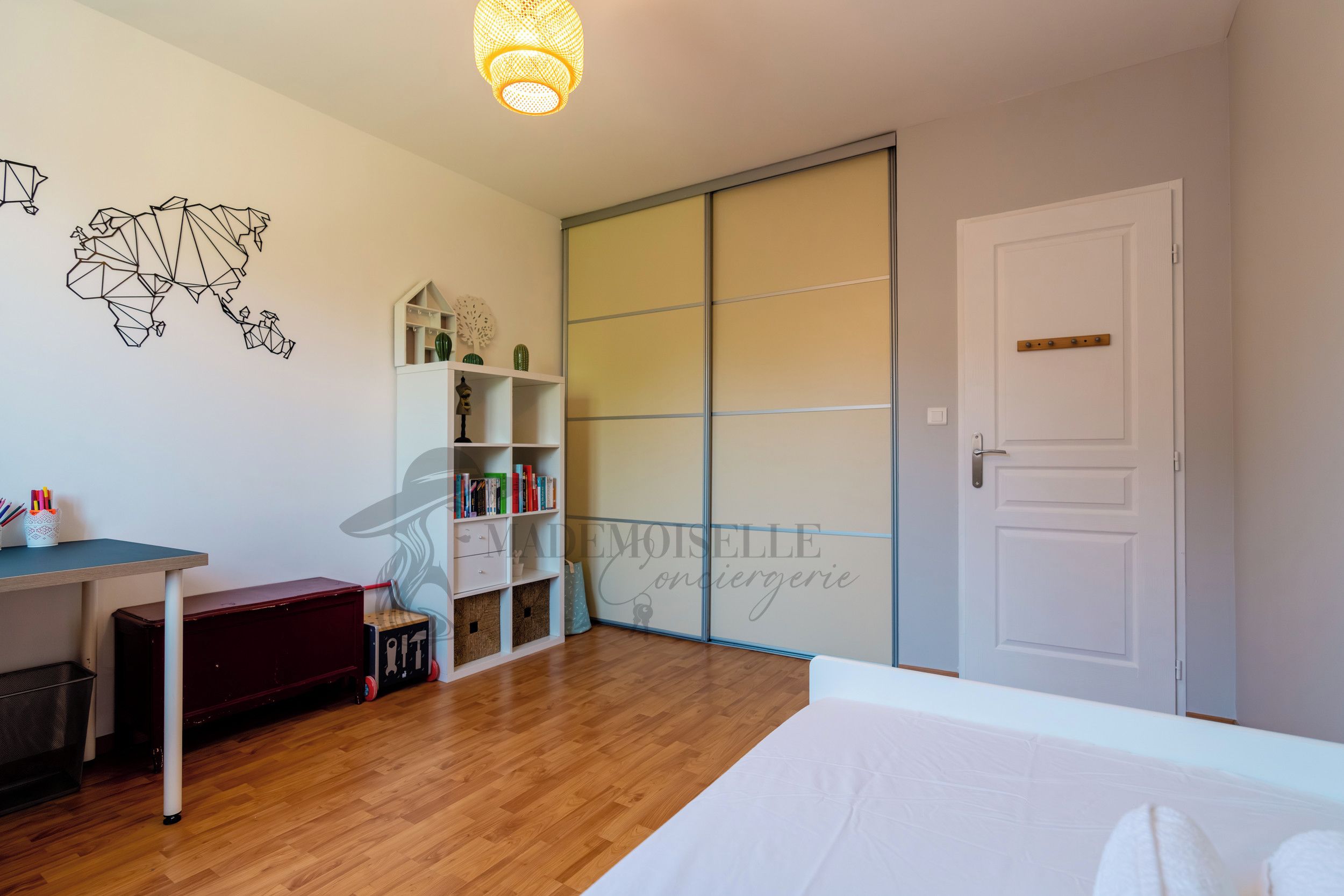 A bedroom with a wooden floor, a bed, a desk, a bookshelf, and a wardrobe.