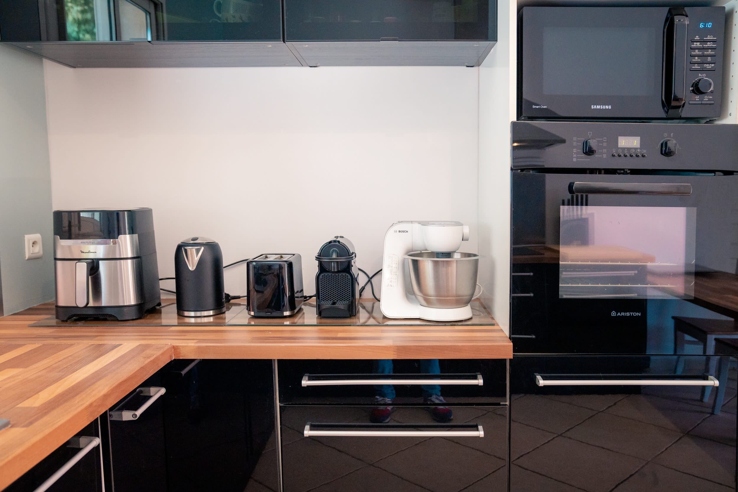 Eine Küche mit Mikrowelle, Backofen, Kaffeemaschine, Toaster und Mixer auf einer Holzausziehtischplatte.