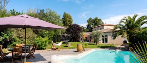 A swimming pool with a wooden deck, a hammock, and outdoor furniture.