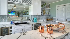 Una cocina moderna con armarios blancos, encimera de mármol y tazas de cobre.