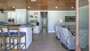 Una cocina amplia con techo de madera, un comedor con sillas de madera, una sala de estar con sofá estampado y un pasillo que conduce a un dormitorio.