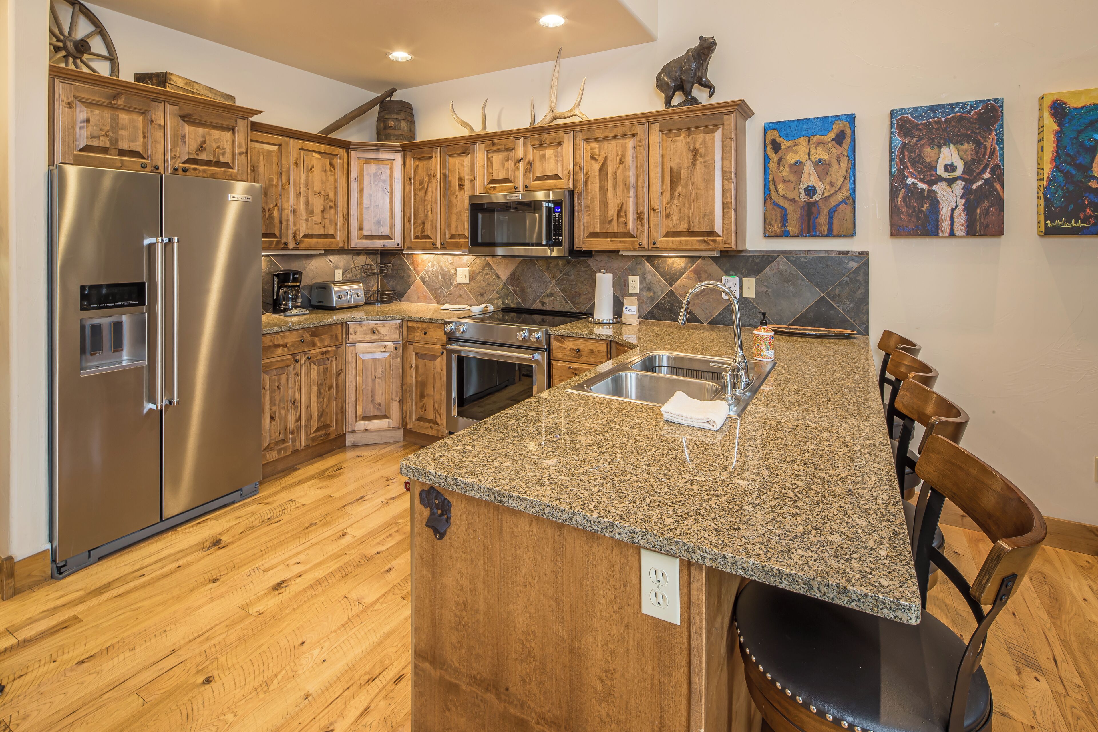 A kitchen with wooden cabinets, stainless steel appliances, granite countertops, and bear-themed artwork.