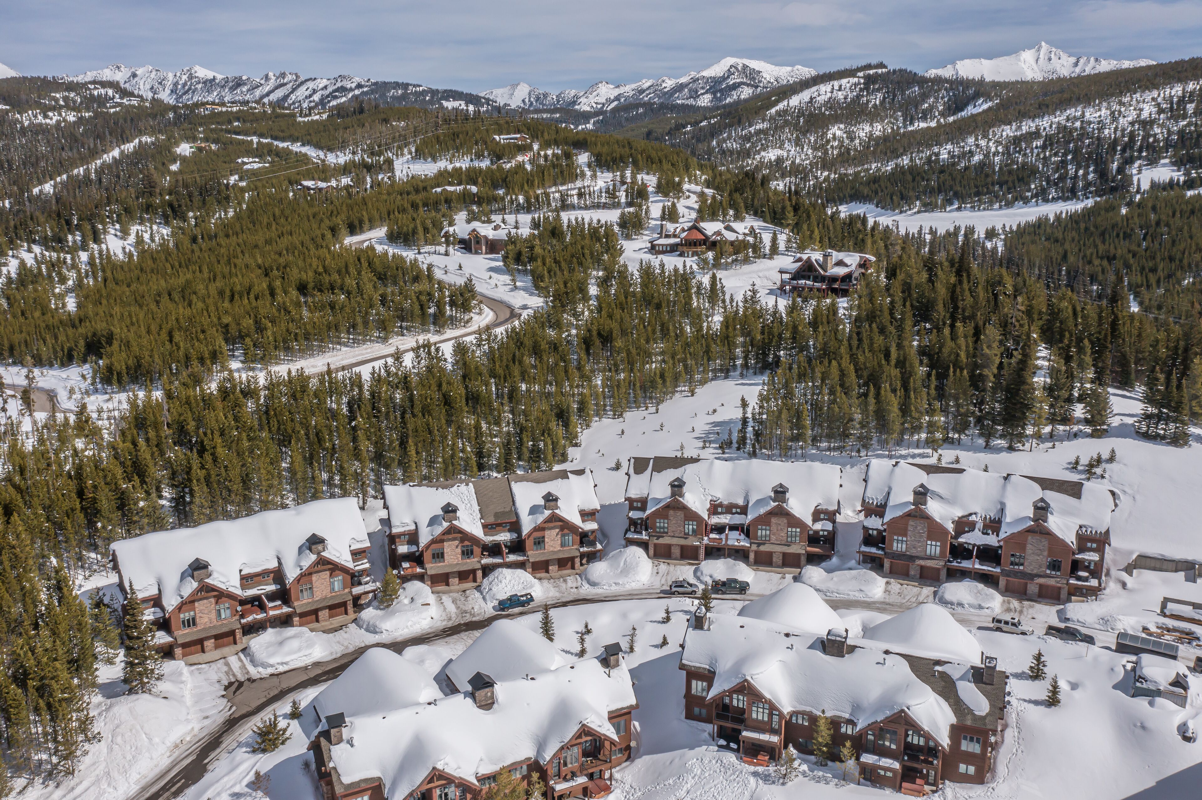Un complejo de esquí con varias edificaciones tipo chalet, techos cubiertos de nieve y montañas al fondo.