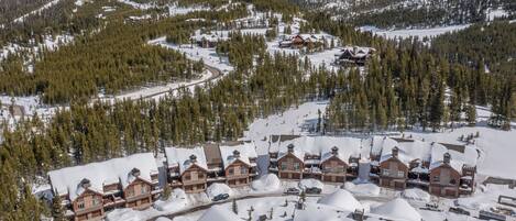 Un complejo de esquí con varias edificaciones tipo chalet, techos cubiertos de nieve y montañas al fondo.