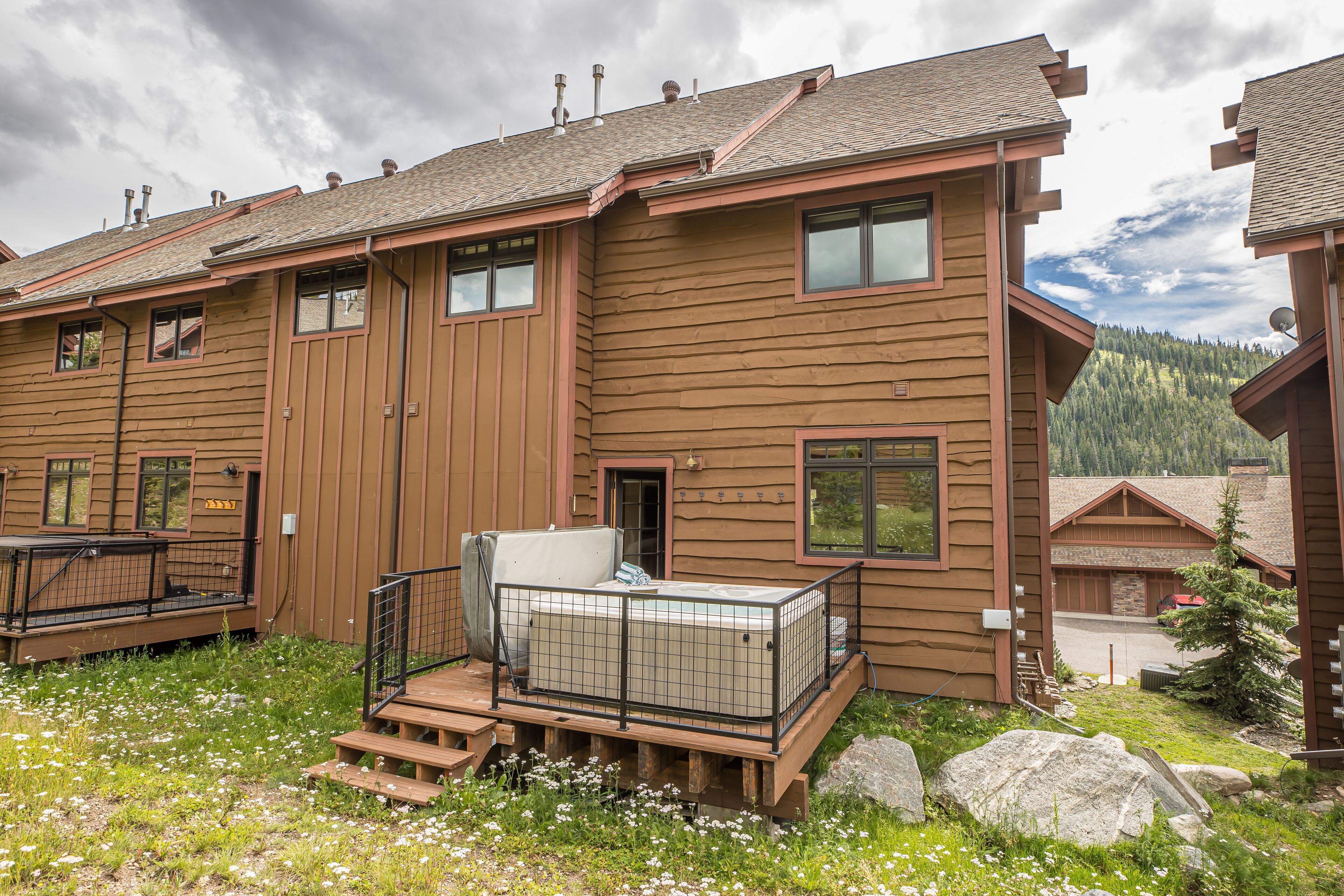 A wooden cabin with a deck, a hot tub, and a view of a forested mountain.