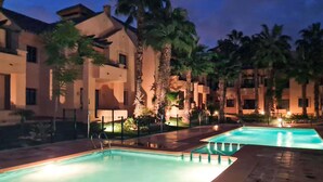 A pool area with two swimming pools, palm trees, and a building with balconies.
