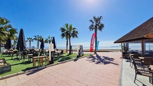 An outdoor seating area with tables and chairs, palm trees, and a clear view of the ocean.