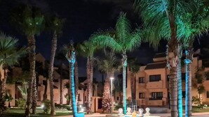 A nighttime view of a resort with palm trees and a fountain.