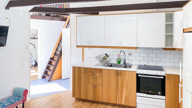 A modern kitchen with wooden cabinets, white upper cabinets, a stainless steel sink, and a built-in oven.