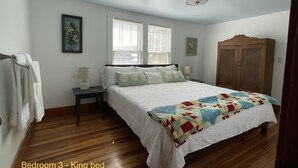 Een slaapkamer met een tweepersoonsbed, twee nachtkastjes, een houten garderobe en een raam met jaloezieën.