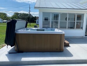 A wooden hot tub with a cover, positioned on a concrete patio in front of a house with large windows. - Central access to all of the wonders of the Shenandoah Valley! (Shenandoah)