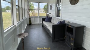 Een achterterras met een grijze bank, een kleine tafel en een decoratieve wandversiering.