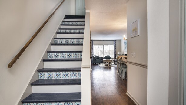 Una escalera con escalones de diseño azul y blanco conduce a un espacio de estar con piso de madera y una mesa de comedor.