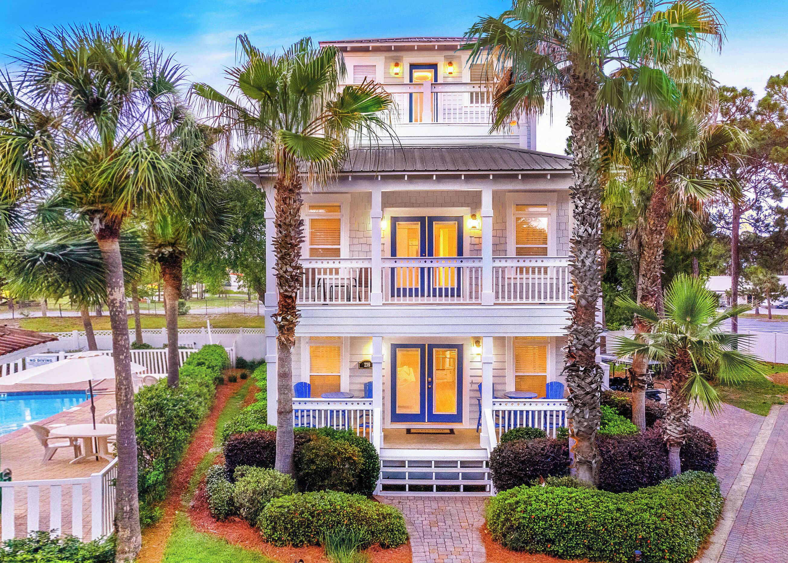 A two-story building with a balcony, surrounded by palm trees and a swimming pool.