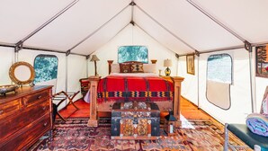 A tented room with a bed, wooden dresser, and a chest of drawers.
