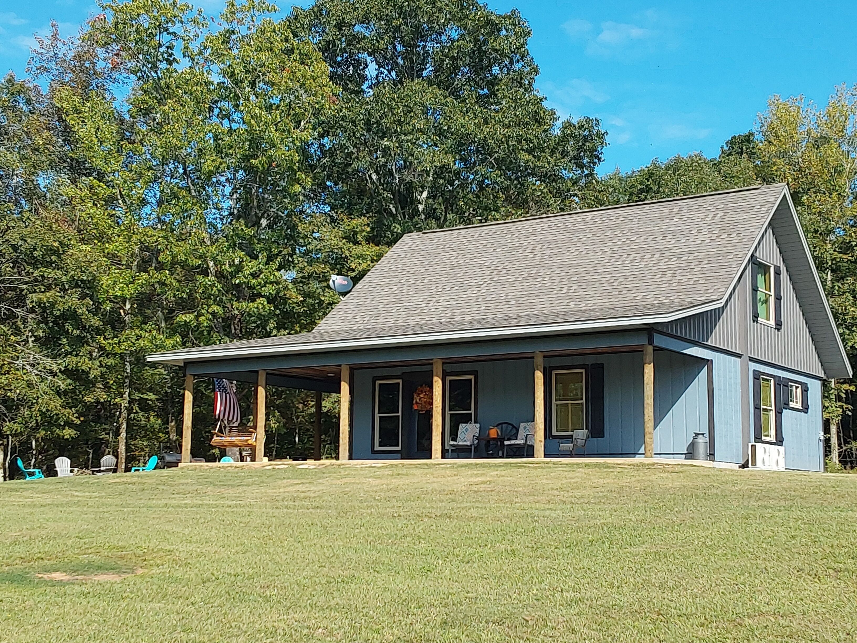 A two-story house with a porch, surrounded by a grassy lawn and trees.