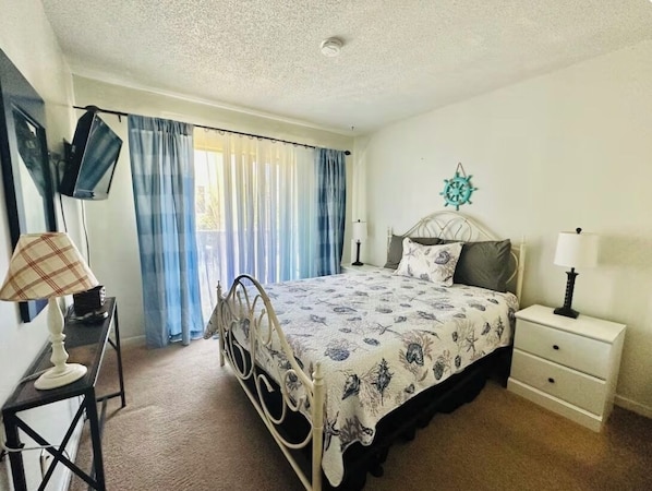 A bedroom with a bed, bedside tables, a desk, a chair, a window with curtains, and a wall decoration.