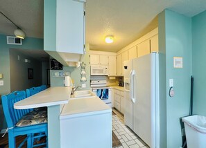 Una cucina compatta con zona pranzo, elettrodomestici bianchi e un cestino.