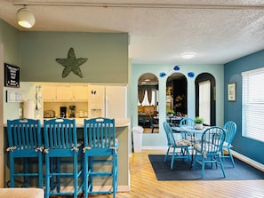 A dining area with blue chairs and a table, a kitchen with white cabinets, and a star decoration on the wall. - Cozy 2 Bedroom condo unit • 5mins walk • 2 blocks to the beach (Myrtle Beach)
