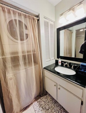 A bathroom with a shower curtain, a sink, a mirror, and a bottle of soap.