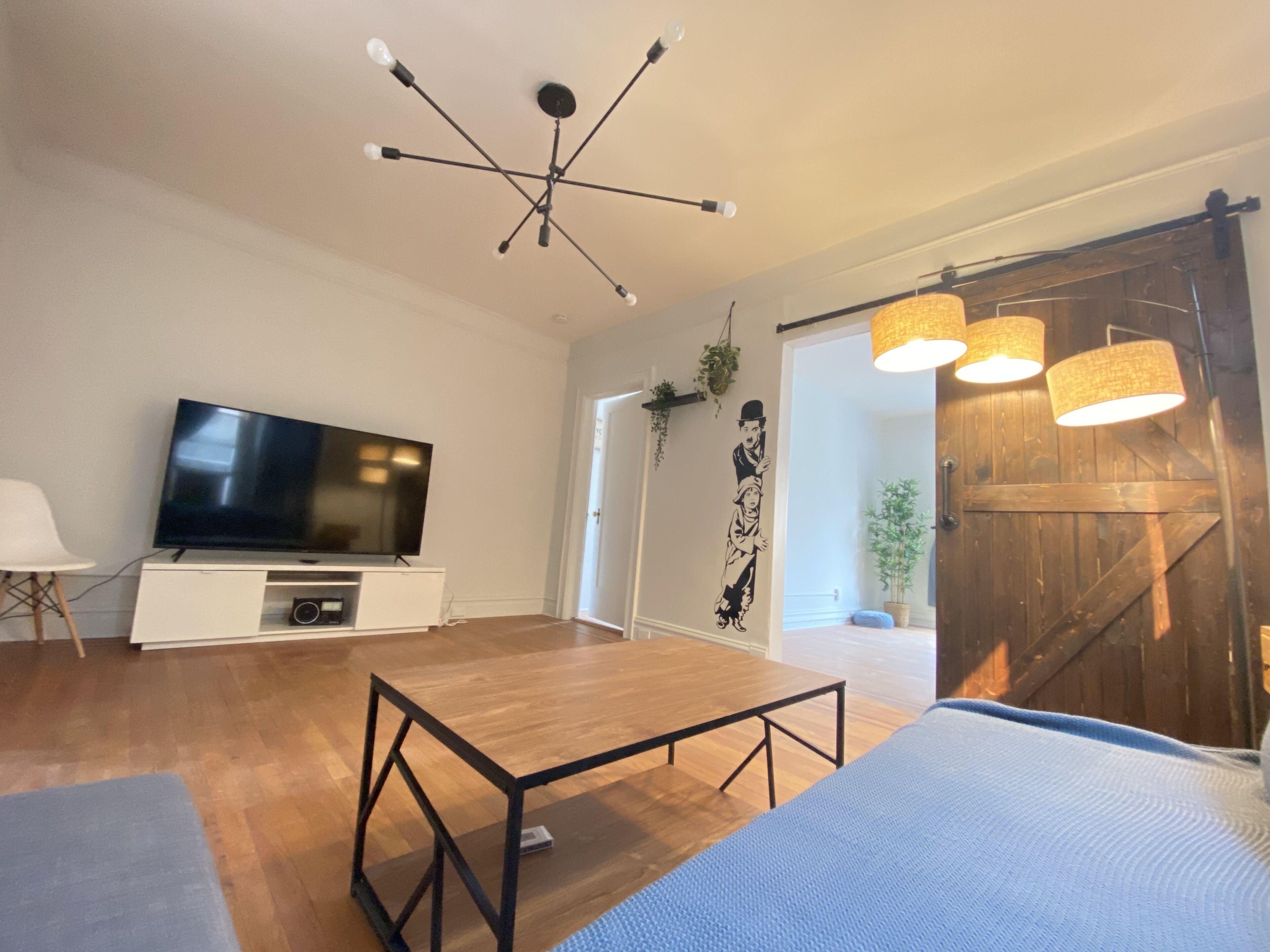 A modern living room with a flat-screen TV, wooden flooring, a dining table, and a large sliding door leading to a balcony.