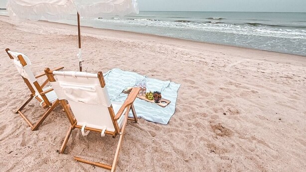 Una playa con una silla de madera y una mesa con una toalla y aperitivos.