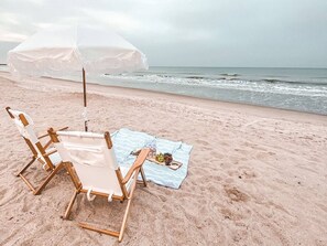 En strand med en trästol och ett bord med en handduk och några snacks.