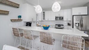 Una cocina moderna con armarios blancos, una isla central con taburetes altos, iluminación colgante y electrodomésticos de acero inoxidable.