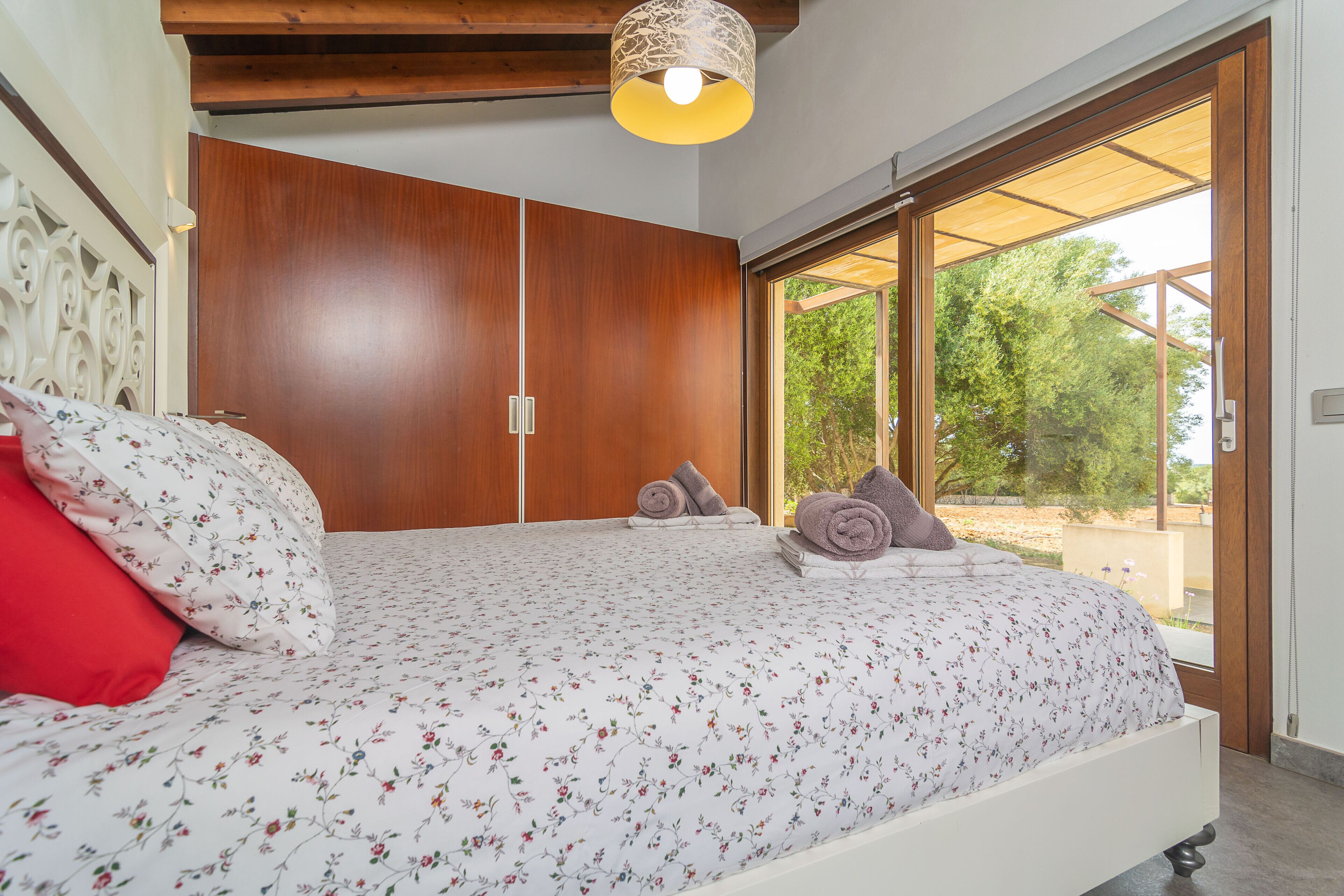 A bedroom with a bed, a wooden wardrobe, and a large sliding glass door leading to an outdoor area.