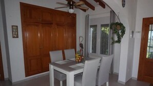 A dining area with a white table and chairs, a wooden door, and a window with a plant. - CASA JOSI with awesome views to the sea at Monte Pego (Pego)