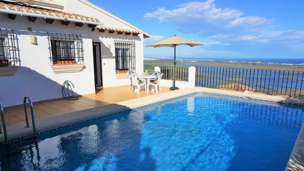 A swimming pool with a view of the sea, a patio with a table and chairs, and a white building with barred windows. - CASA JOSI with awesome views to the sea at Monte Pego (Pego)