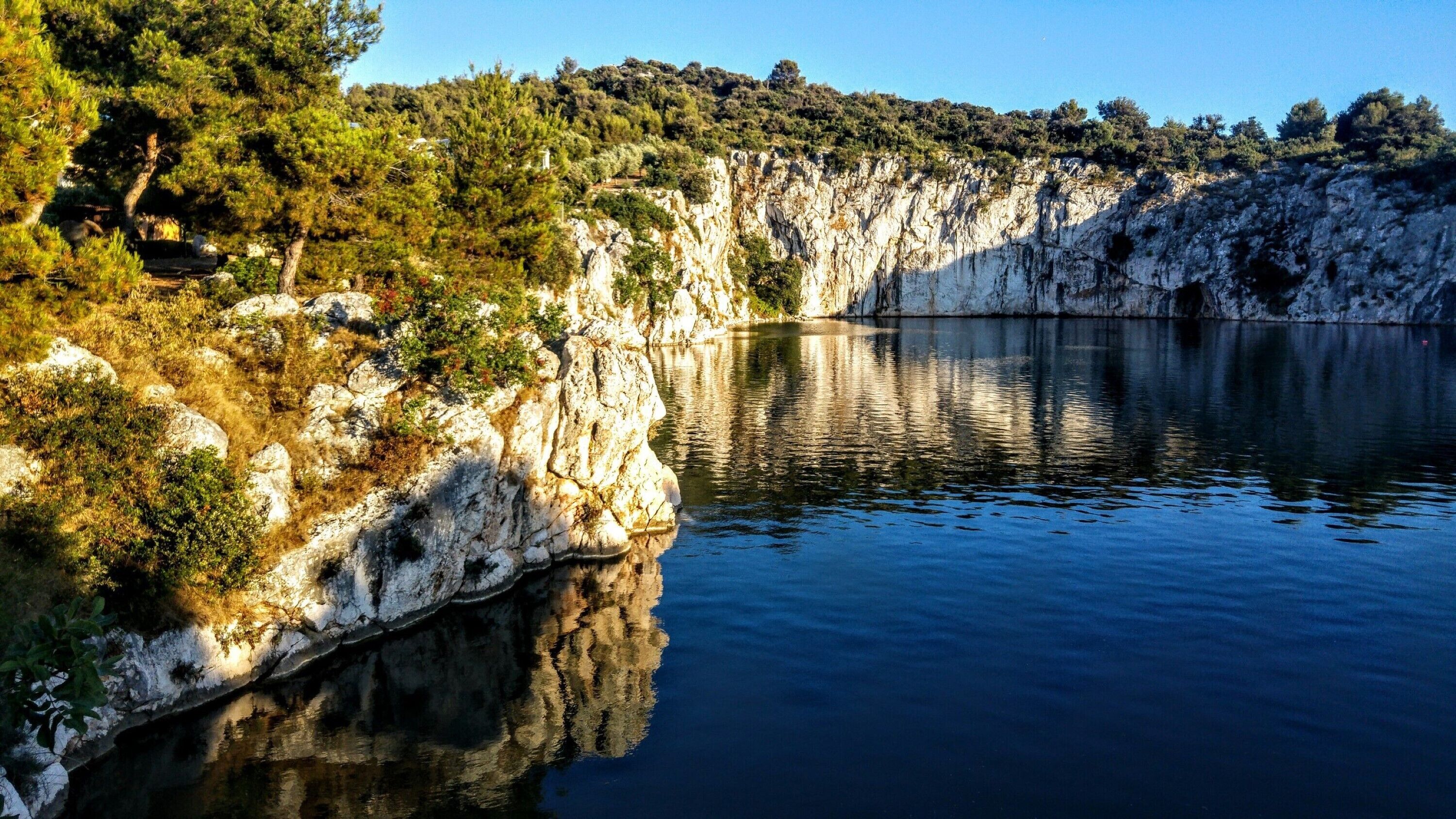 A serene lake with rocky cliffs and dense greenery.